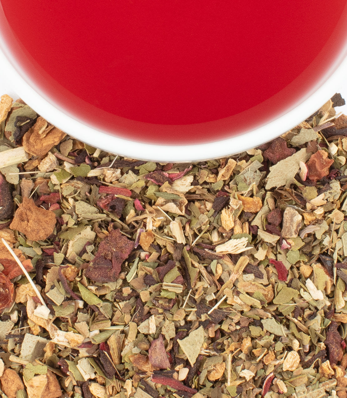 A close-up of organic hibiscus ginger tea leaves beside a vibrant red cup of brewed tea.