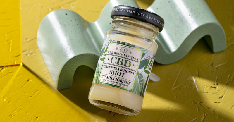 CBD shot glass with green tea and honey flavor on a yellow surface.