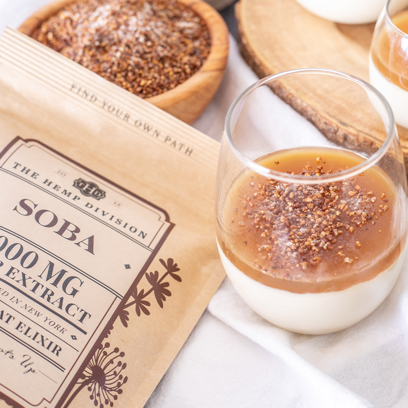 Soba Elixir 1,000 MG CBD in a glass, topped with a sprinkle of seeds, alongside a wooden bowl and packaging.