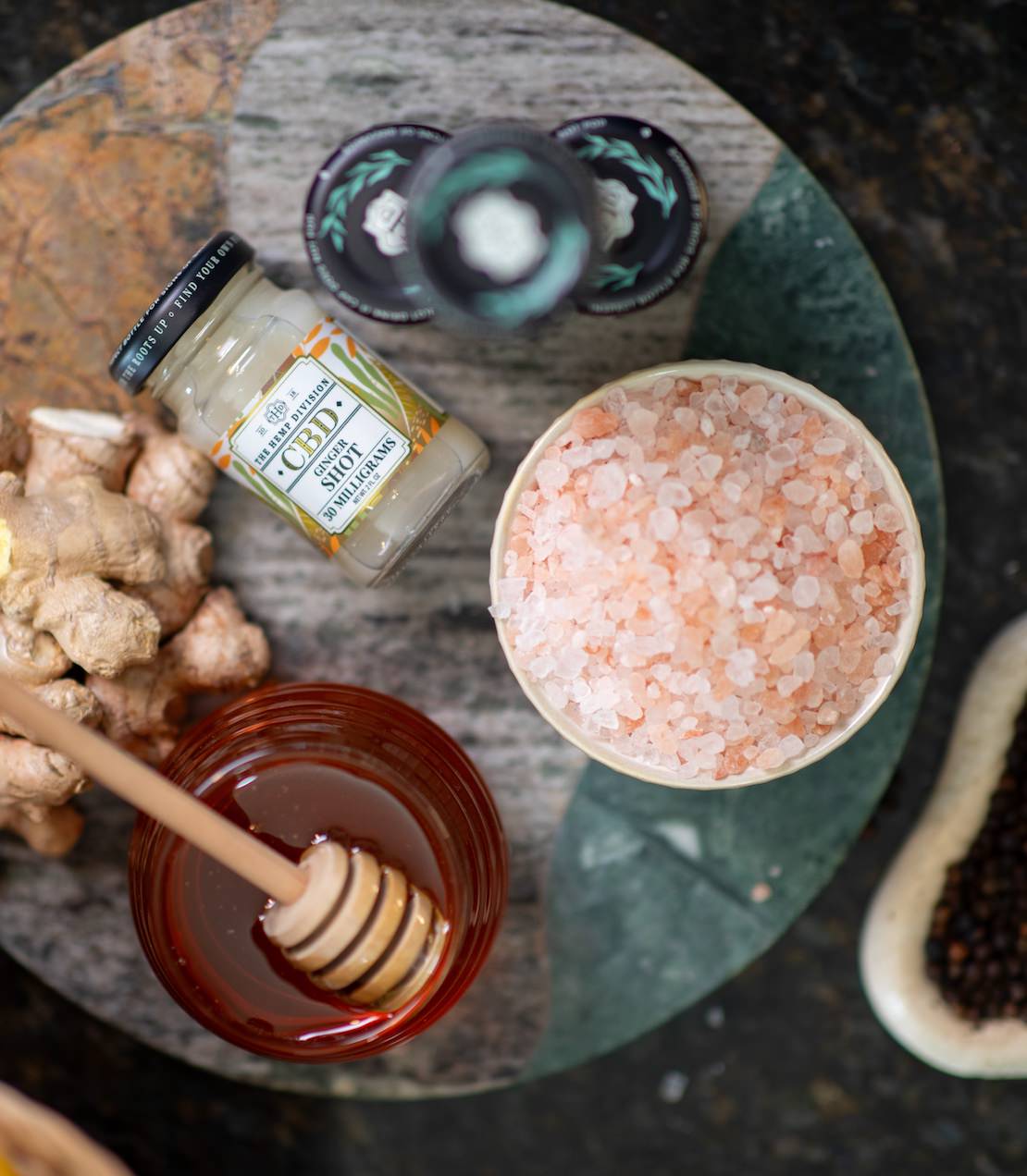 Ginger CBD shot laying on a marble surface next to honey, ginger, and sea salt.