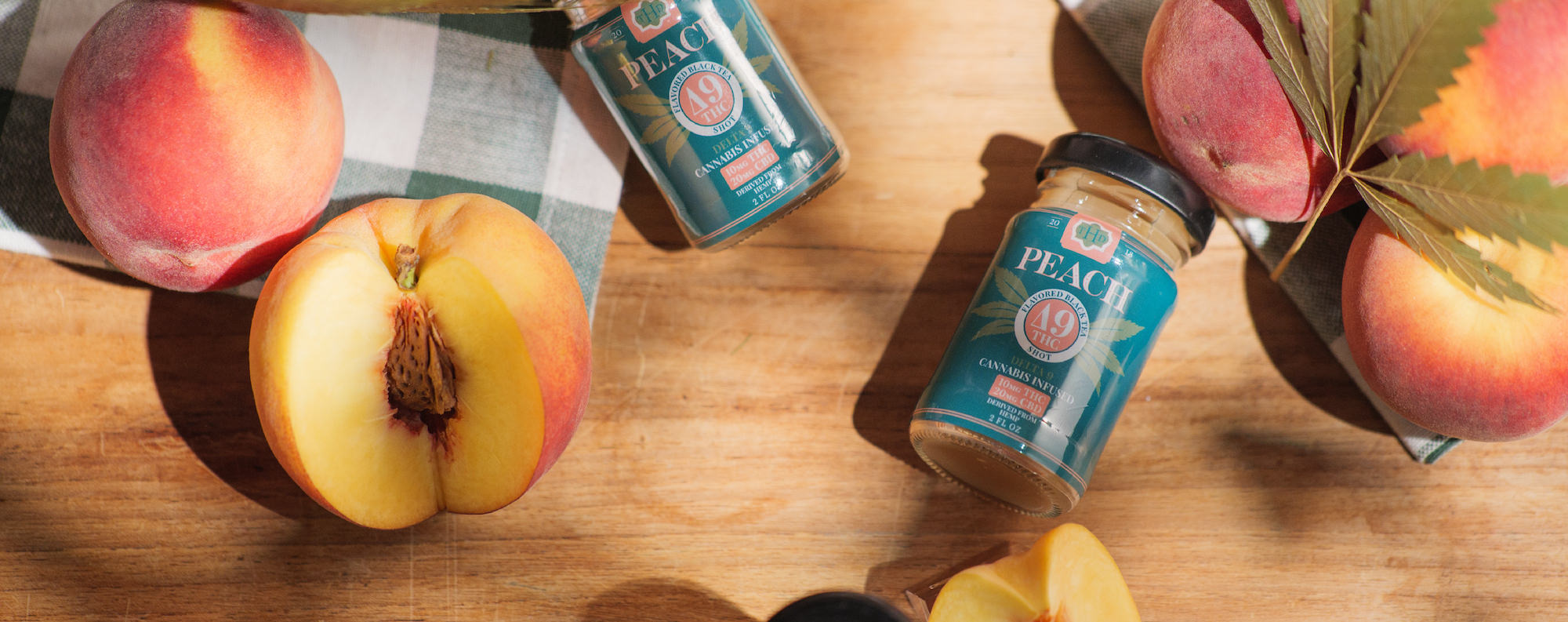 Peach Tea Shot sitting on table with peach fruit and cannabis leaves around it.